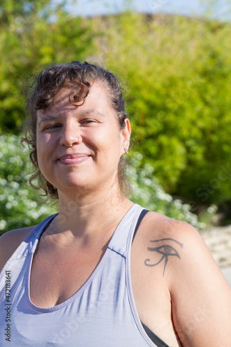 Portrait of happy woman with curly hair doing sports. Chubby woman in blue top with tattoos proudly looking at camera. Sport, body positive concept