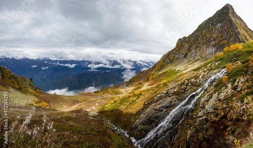 Mountain valley autumn cloudy landscape with waterfall and snow