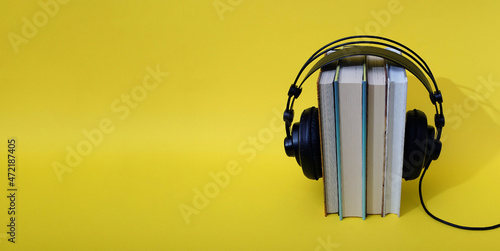 Books set upright with black headphones on top on a yellow background. Text space. Audio book concept. Minimal style.