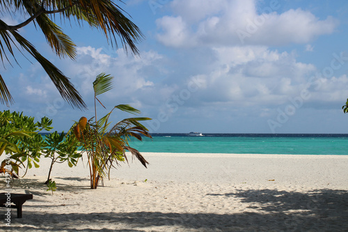 View of the Indian Ocean coast with trees, white sand, azure water, in which a ship is sailing, in the Maldives