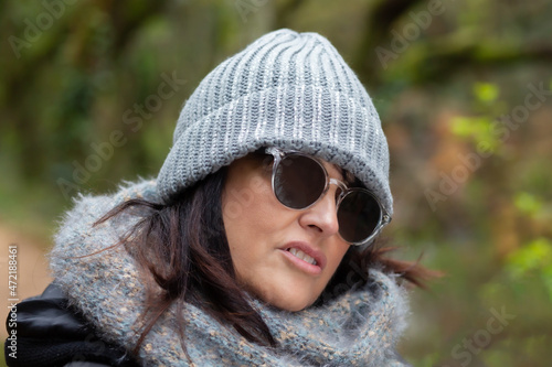 portrait of a woman with sunglasses and wool hat in the forest on an autumn day in the morning - close-up portrait 