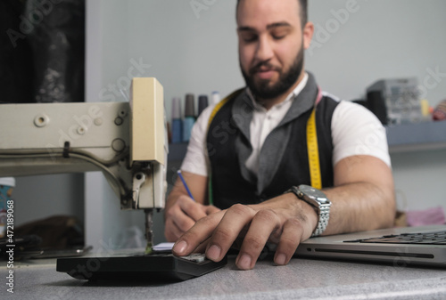 Tailor shop owner calculating monthly reports, bills and expenses of his small business.  Small entrepreneurship photo