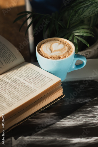 Cappuccino coffee in a blue ceramic mug in the sunbeams in a light cafe with a book in his hands
