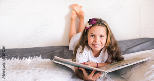 Schoolgirl reading a book in the room. Girl 8 or 10 years old with a book in the room on the bed. A child in a bright interior to study at home. Copy space. Banner. High quality photo