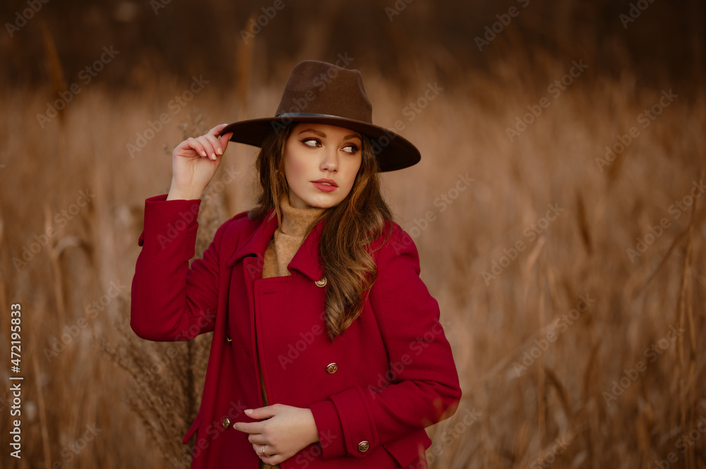 Elegant confident lady wearing stylish brown hat, red marsala color classic coat posing in nature. Model looking aside. Outdoor autumn portrait. Copy, empty space for text Elegant confident lady wearing stylish brown hat, red marsala color classic coat posing in nature. Model looking aside. Outdoor autumn portrait. Copy, empty space for text