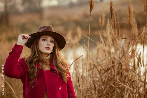 Outdoor autumn portrait of elegant woman wearing stylish brown hat, red marsala color classic coat posing in nature. Copy, empty space for text © Victoria Fox