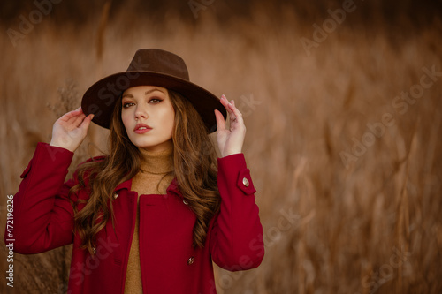 Outdoor autumn fashion portrait of elegant woman wearing trendy brown hat, red marsala color classic coat posing in nature. Copy, empty space for text © Victoria Fox