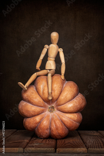 A wooden gestalt mannequin is engaged with a pumpkin on a wooden table and an art background for Halloween.