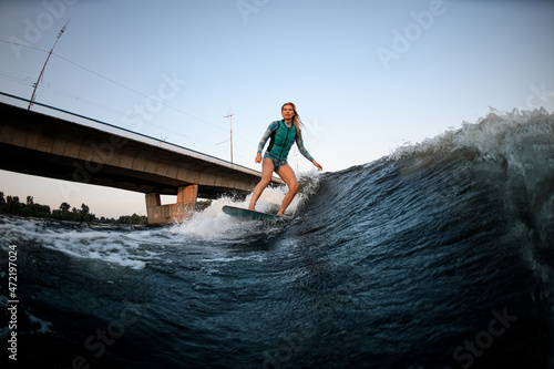 active woman wakesurfer riding down the great splashing river wave.