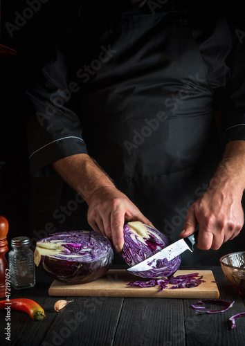 Professional chef is cutting red cabbage with a knife. Cooking vegetable salad in the restaurant kitchen. Vegetable diet idea.