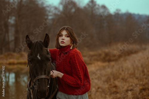 Outdoor autumn portrait of elegant fashionable woman wearing stylish knitted turtleneck sweater posing with horse in nature. Copy, empty space for text photo