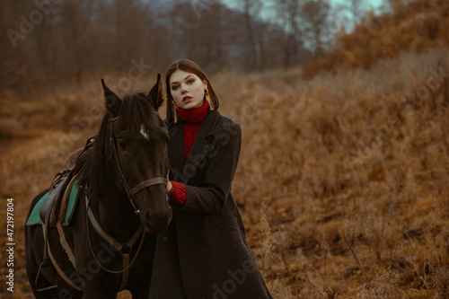 Elegant confident fashionable woman wearing classic grey woolen  coat  posing with horse in nature. Outdoor autumn fashion portrait. Copy, empty space for text © Victoria Fox