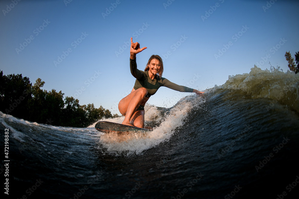 cheerful woman sits on surf rides and touches waves with one hand and show hand gesture