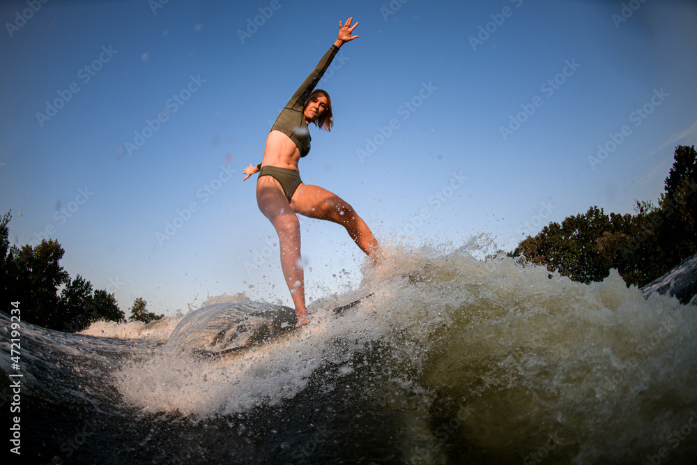Healthy athletic woman balancing on wakesurf board on the river wave