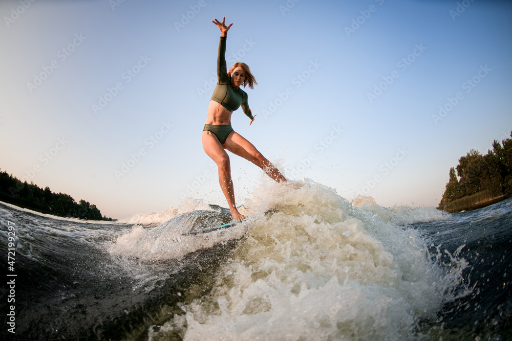 Strong athletic woman balancing on wakesurf board on the river wave