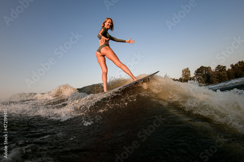 Active slim woman balancing on wakesurf board on the river wave