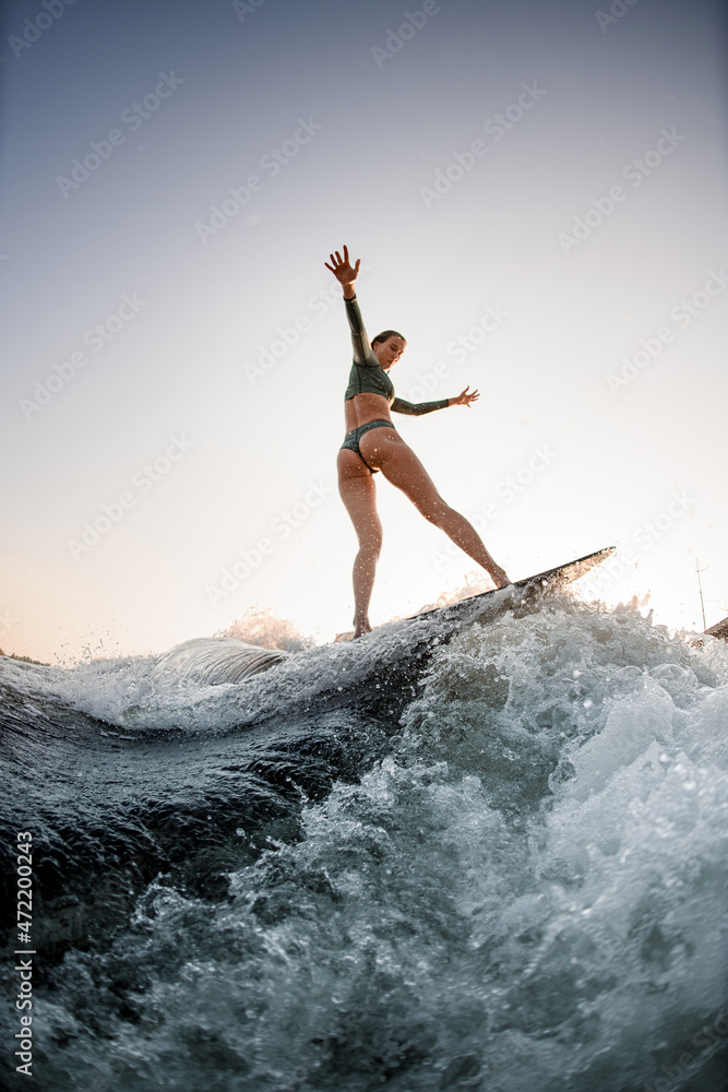 sexy wet woman wakesurfing on the board on the river wave against blue sky