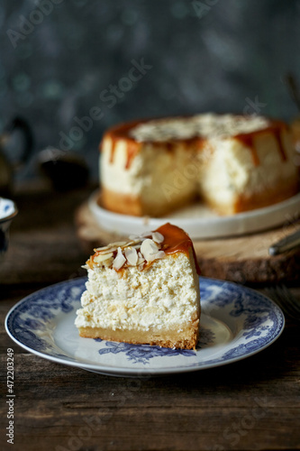 cheesecake with caramel and almonds on a white plate and a wooden board. Side view, green and wooden background.