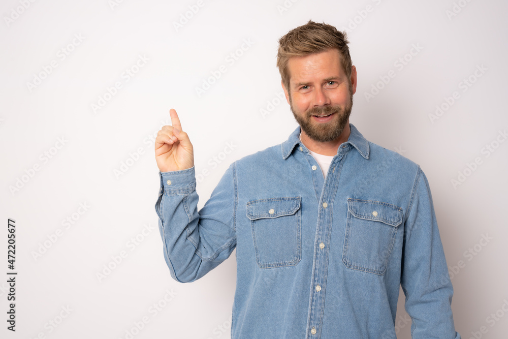 Young smiling man in denim shirt pointing finger up isolated over white background. Young smiling man in denim shirt pointing finger up isolated over white background.