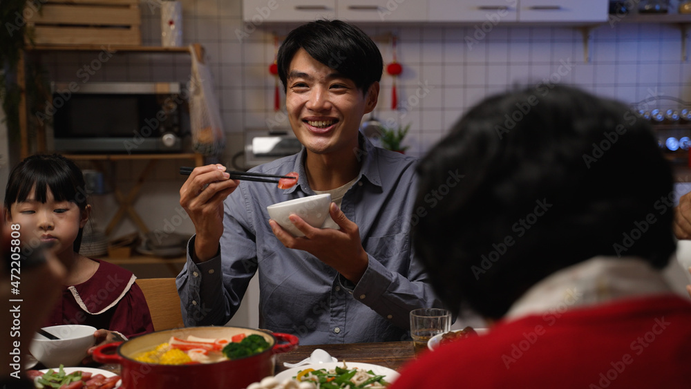 selective focus smiling asian father talking to family while enjoying tasty food at dinner table. people chatting happily during reunion meal on lunar new year’s eve at home - obrazy, fototapety, plakaty 
