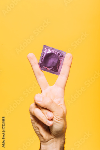 Man with condom packet gesturing against yellow background