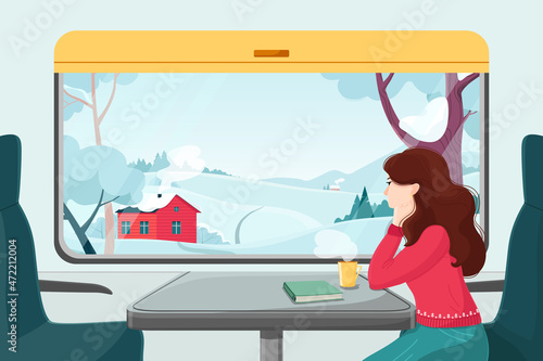 A girl in a red sweater looks out the window at the winter landscape. Traveling by train. A view of the village landscape with houses, forest and fields. A ride in a train carriage for the New Year