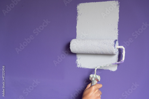 Hand applying light color paint to wall and copy space
