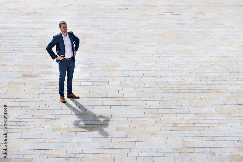 Young male professional standing with hands on hip on footpath Young male professional standing with hands on hip on footpath