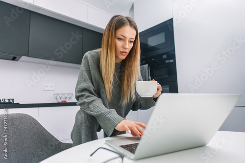 Young woman typing on laptop and holding a mug with coffee