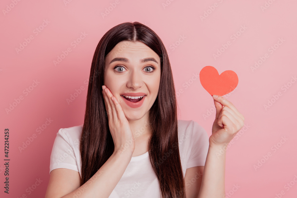 Portrait of attractive lovely cheerful amazed surprised hold small little heart isolated over pink background Portrait of attractive lovely cheerful amazed surprised hold small little heart isolated over pink background