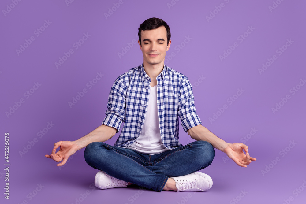 Full body photo of young guy sit floor yoga meditation om dream isolated over violet color background Full body photo of young guy sit floor yoga meditation om dream isolated over violet color background