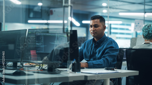 In Diverse Office: Portrait of Handsome Indian Man Working on Desktop Computer. Professional Programmer Creates Innovative Software, Modern App Design. Stylish Multi-Ethnic Authentic Workplace