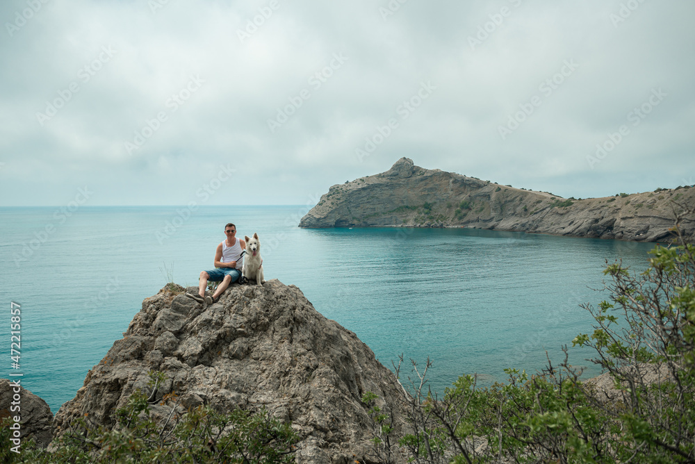 A man is sitting on a huge stone with a white dog. View of the Black Sea coast, Cape Kapchik