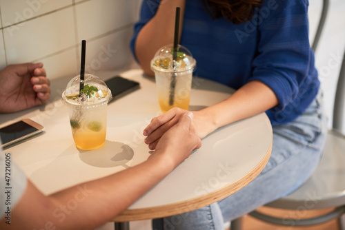 Close-up of unrecognizable couple holding hands on table with lemonade and smartphones in cafe