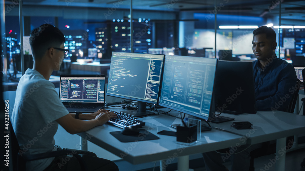 Night Office: Young Japanese Man in Working on Desktop Computer. Diverse Multi-Ethnic Team of Programmers Typing Code, Creating Modern Software, e-Commerce App Design, e-Business Programming. Night Office: Young Japanese Man in Working on Desktop Computer. Diverse Multi-Ethnic Team of Programmers Typing Code, Creating Modern Software, e-Commerce App Design, e-Business Programming.