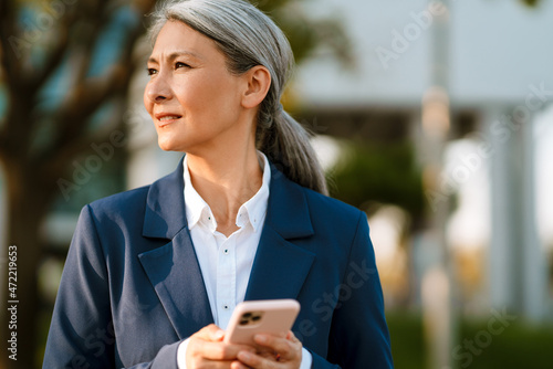 Grey asian woman wearing blue jacket using mobile phone