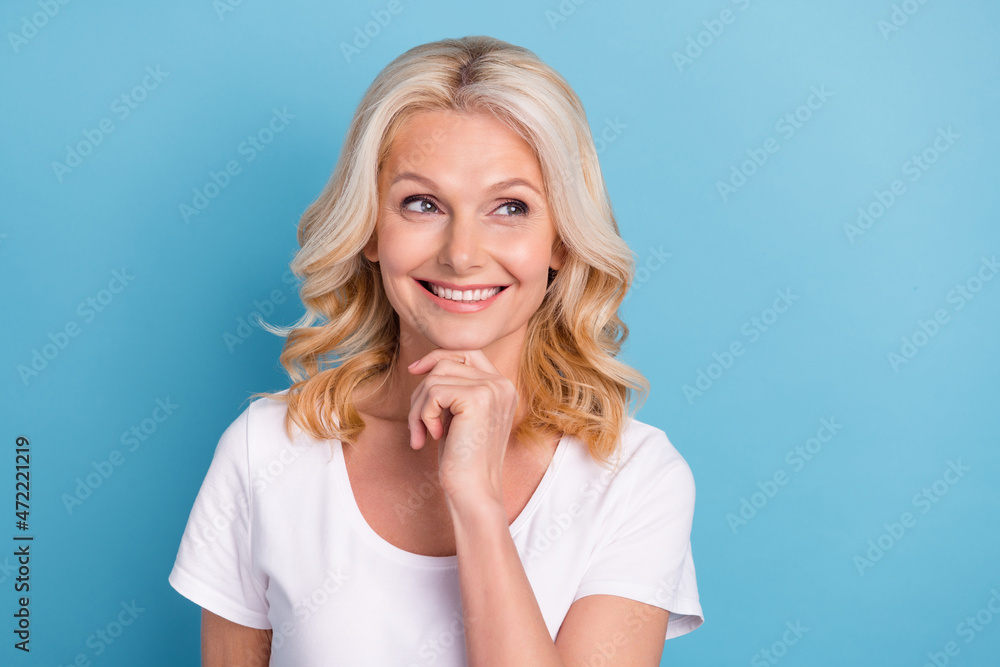 Photo of mature woman happy positive smile hand touch chin curious look empty space isolated over blue color background Photo of mature woman happy positive smile hand touch chin curious look empty space isolated over blue color background