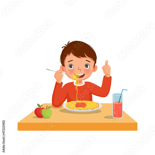 Cute little boy eating delicious spaghetti using fork showing thumb up gestures


