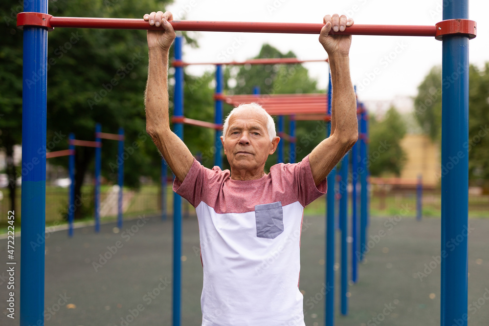 Active grandpa pulls up on horizontal bar on sports ground Active grandpa pulls up on horizontal bar on sports ground