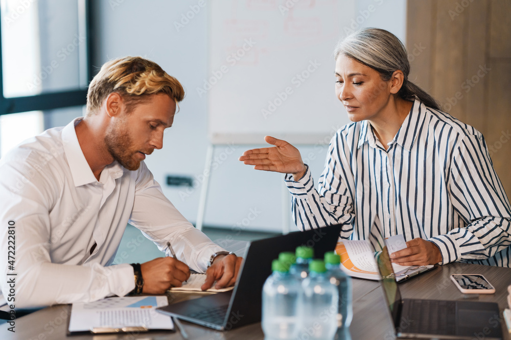 Multiracial men and women discussing project during meeting in office Multiracial men and women discussing project during meeting in office