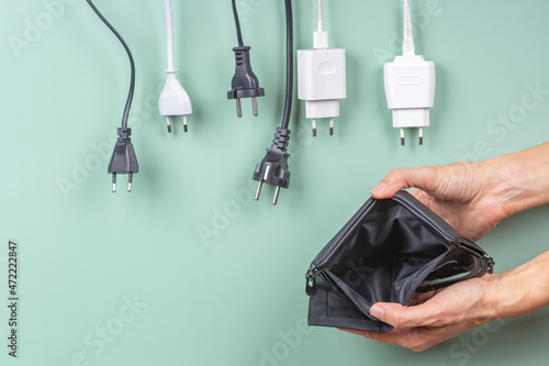 Many power cable cords hanging over empty open wallet in woman hands. Electric power consumption, electricity cost, and expensive energy concept photo
