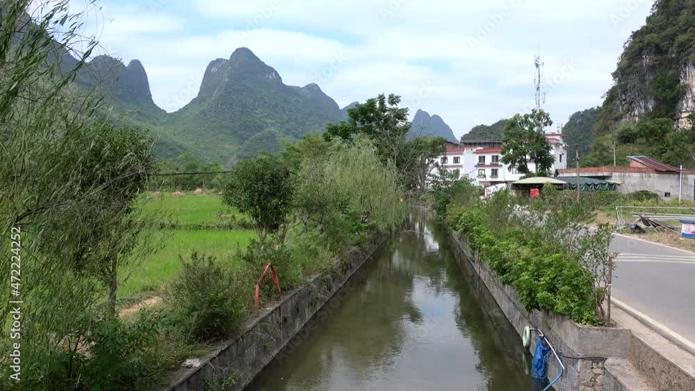 Countryside of Yangshuo county with a small settlement, agriculture fields, irrigation stream and karst hills at background. Guilin, Guangxi Zhuang, China Countryside of Yangshuo county with a small settlement, agriculture fields, irrigation stream and karst hills at background. Guilin, Guangxi Zhuang, China