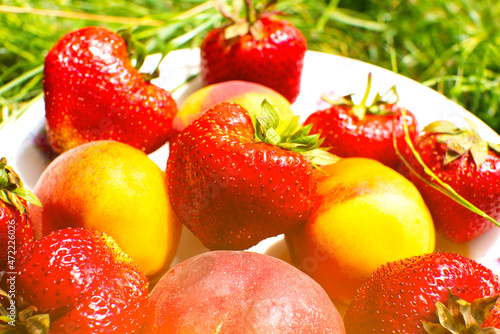 Strawberries and peaches on a plate on the green grass. Delicious and fresh summer fruits. Healthy vegetarian food with vitamins.