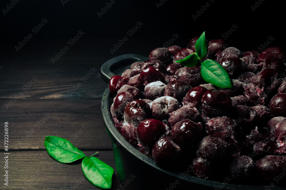Frozen cherry in a bowl with green leaf on wooden black background.Vitamins and a healthy diet Frozen cherry in a bowl with green leaf on wooden black background.Vitamins and a healthy diet