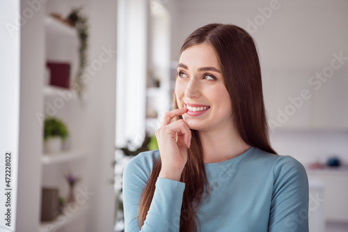 Photo of positive dreamy inspired girl bite finger look up think creative girlish thoughts blue shirt home indoors