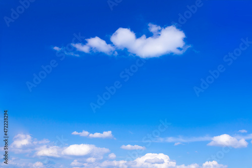 Bright blue summer sky with a few fluffy white clouds, background texture, copy or text space.