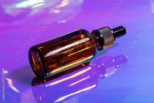 Oily serum in glass bottle with pipette on pink and purple background, neon light with copy space. Modern and futuristic cosmetic