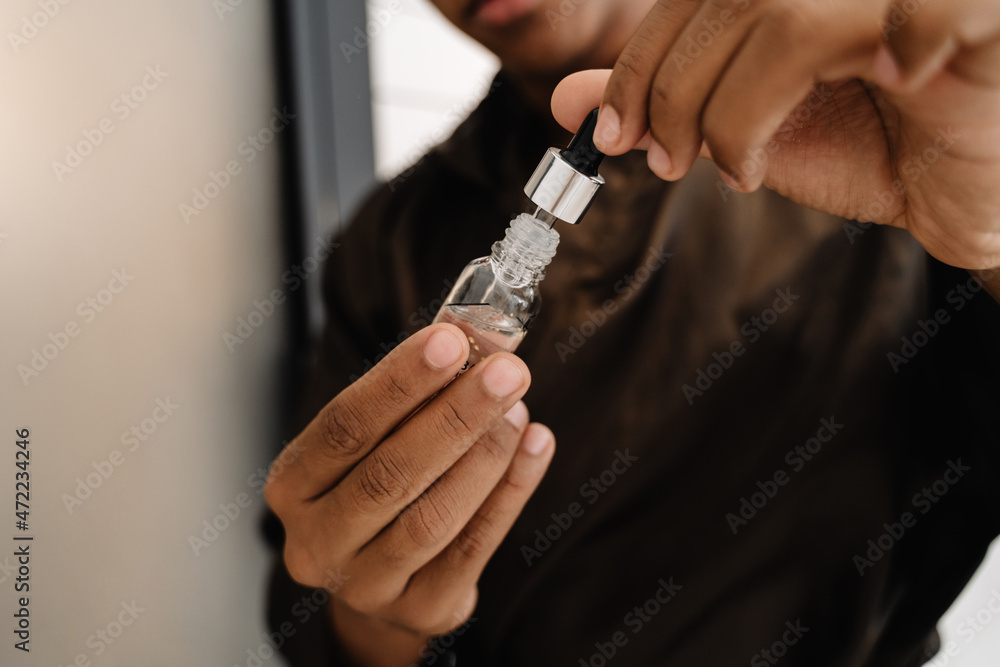 Black man wearing bathrobe applying face serum in bathroom Black man wearing bathrobe applying face serum in bathroom