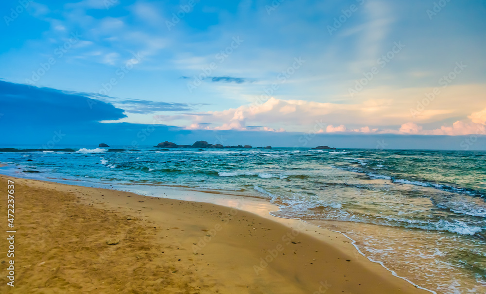 Landscape with a sandy seashore against the sky with clouds in the city of Hikkaduwa in Sri Lanka