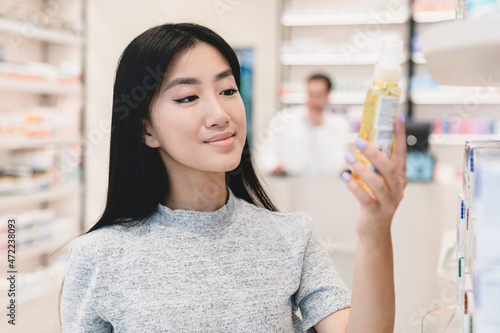Asian female young customer buyer client looking at drug medicine jar, reading ingredients, side effects on pills, painkillers, antibiotics in pharmacy drugstore photo